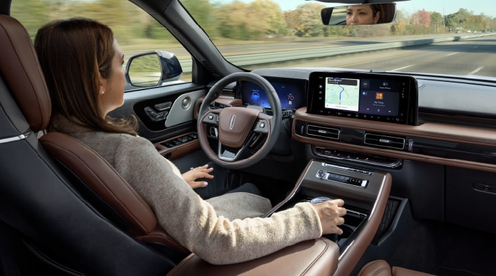 A woman is seen sitting in the driverās seat of her 2025 Lincoln AviatorĀ® SUV with her hands off the steering wheel.