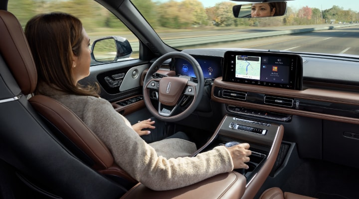 A 2026 Lincoln Aviator<sup>®</sup> SUV is being driven hands-free on a highway near a forest.