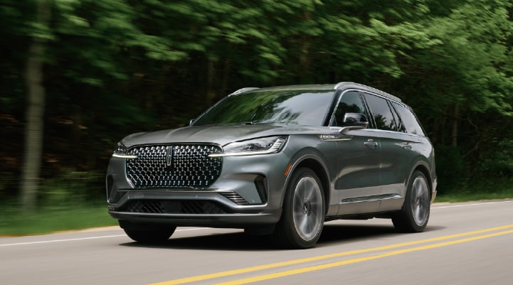 A 2027 Lincoln Black Label™ Aviator® SUV is being driven down a road lined with trees.