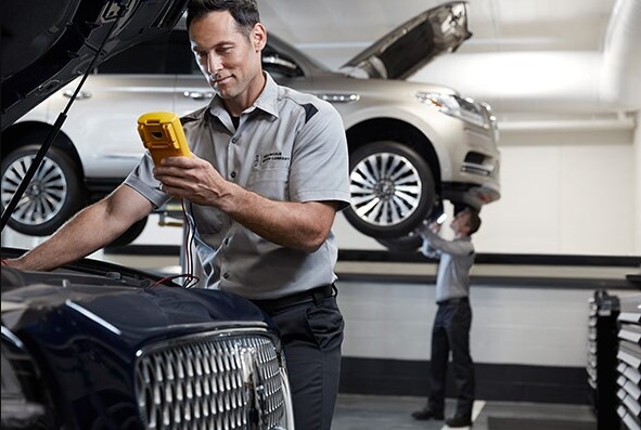 Lincoln of New Bern is a Car Dealership in New Bern near Brices Creek NC | Lincoln service technician inspecting under the hood of silver Lincoln vehicle