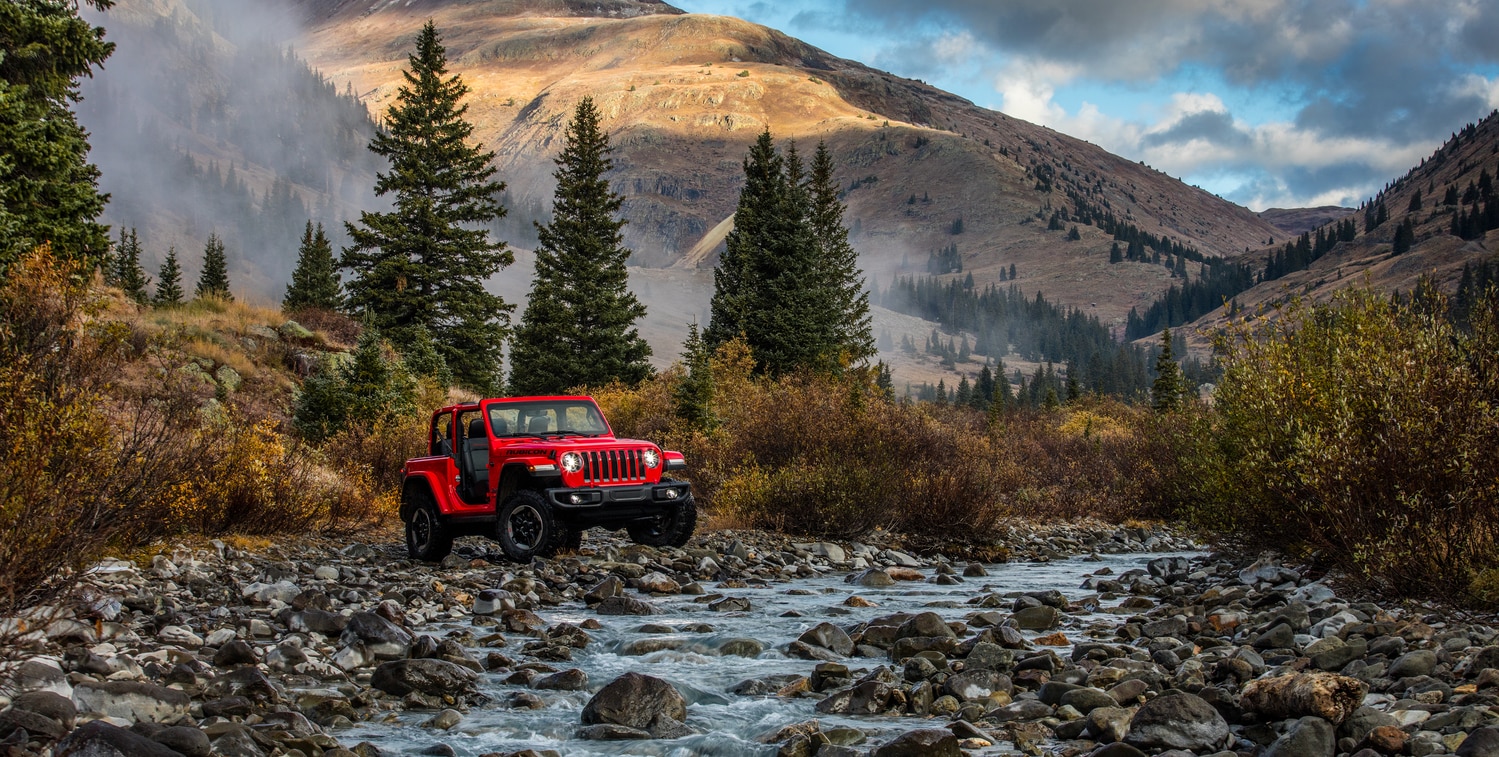 red Jeep Wrangler SUV bouldering in a mountain stream