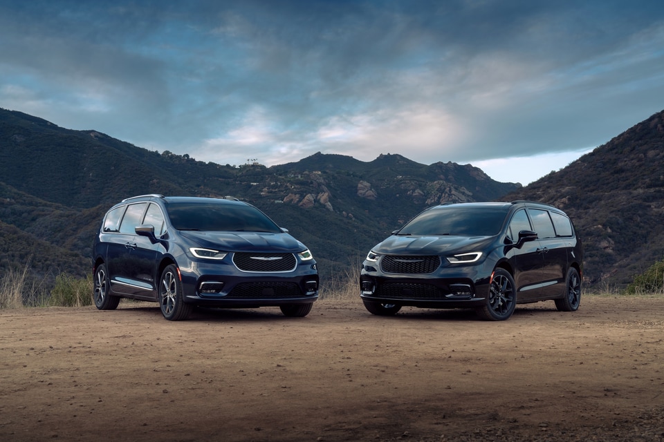blue and black Chrysler Pacifica minivans, parked in front of a mountain range