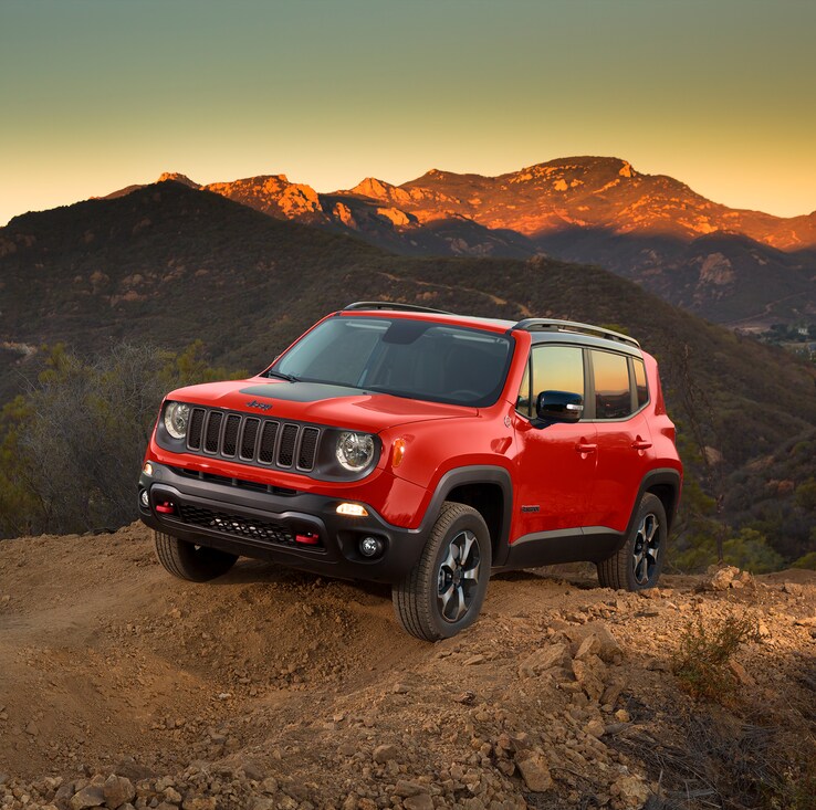 red Jeep Renegade SUV parked on a ledge overlooking hills at sunset