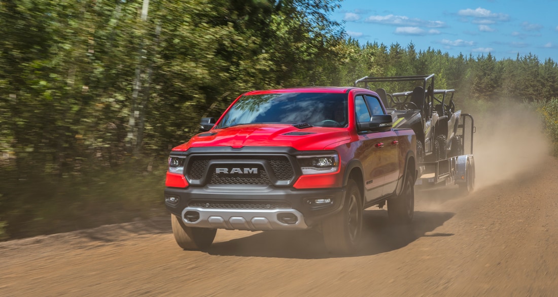 red Ram 1500 Rebel truck towing an ATV and driving fast on a dirt road