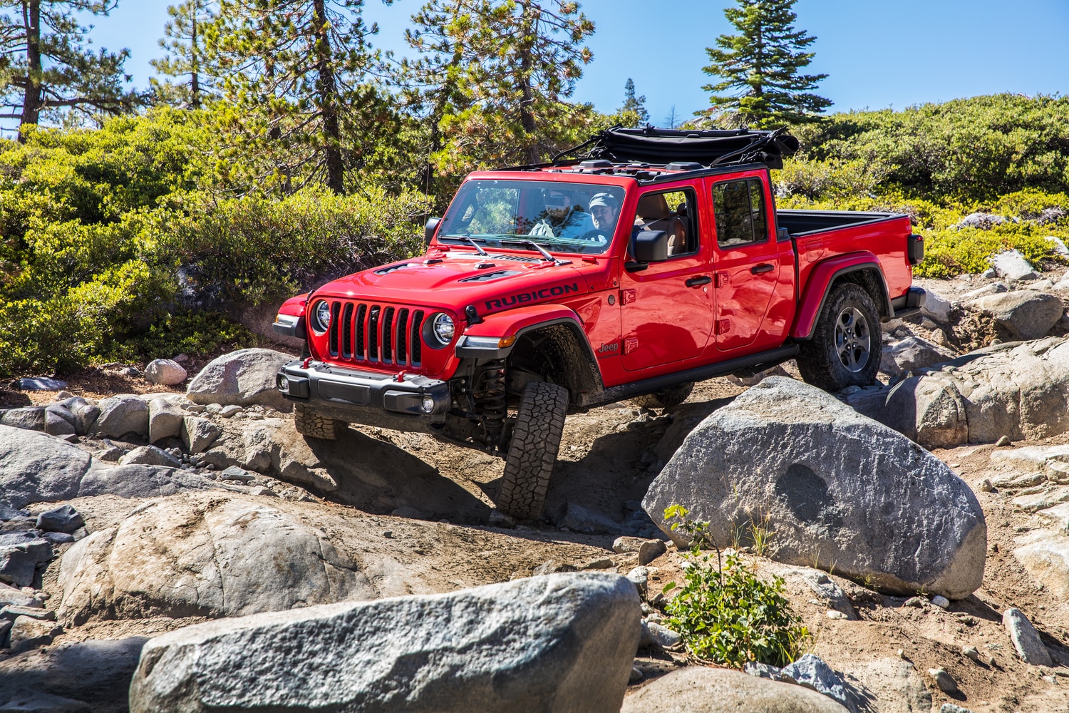 red Jeep Gladiator bouldering over rocks in a forest area