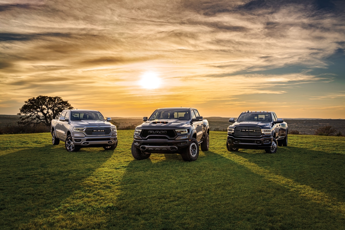Ram 1500 truck lineup with black, blue, and silver trucks parked in front of a sunset