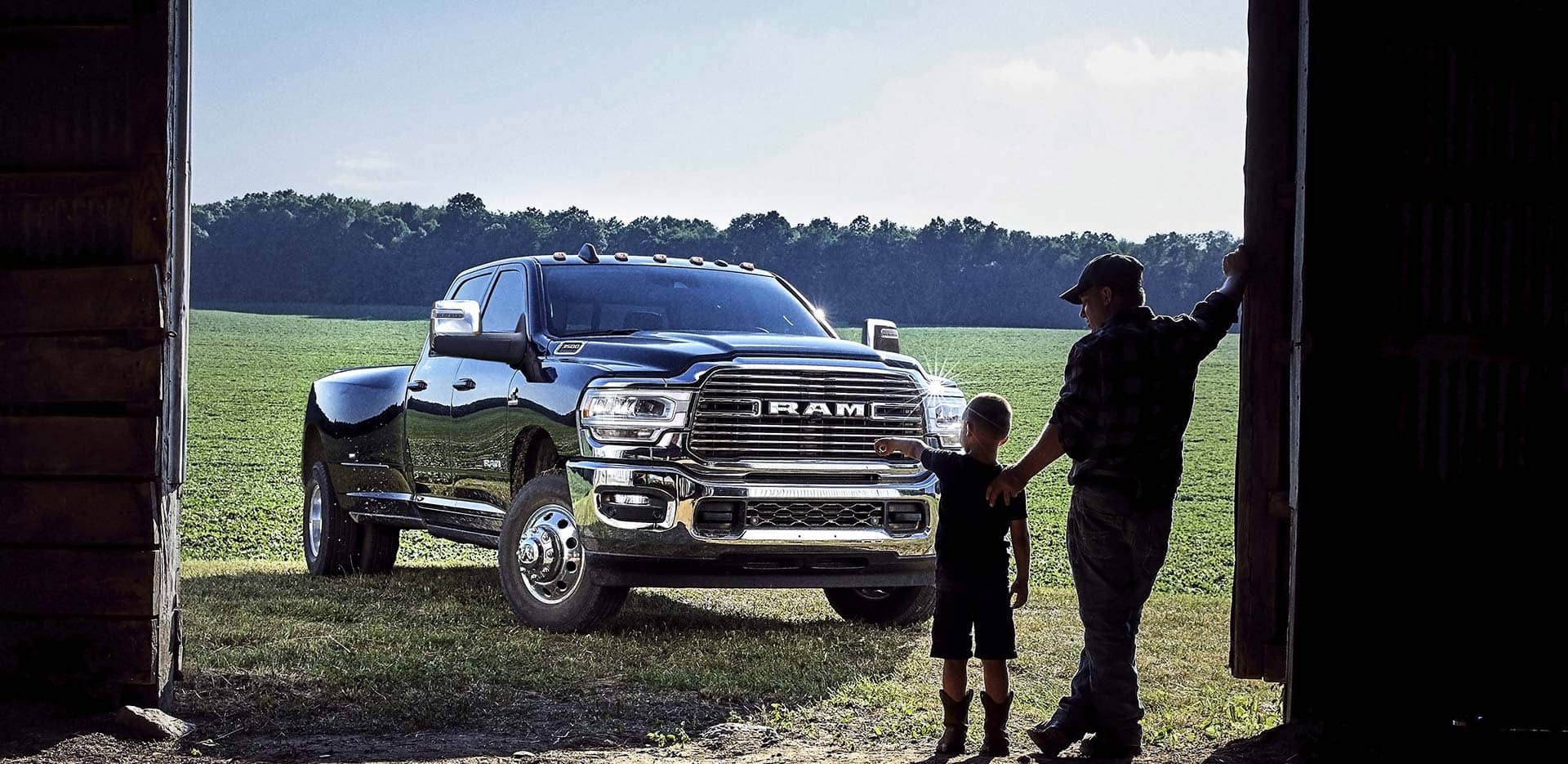 father and son looking out from a barn, with the boy pointing at a Ram 3500 heavy duty truck parked outside