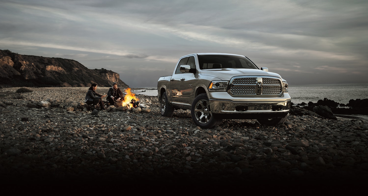 silver Ram 1500 truck parked on a beach with two campers next to a fire