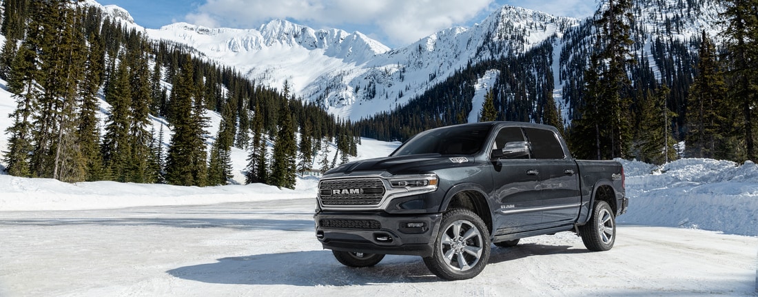 black Ram 1500 truck parked in the snow next to evergreens and mountains