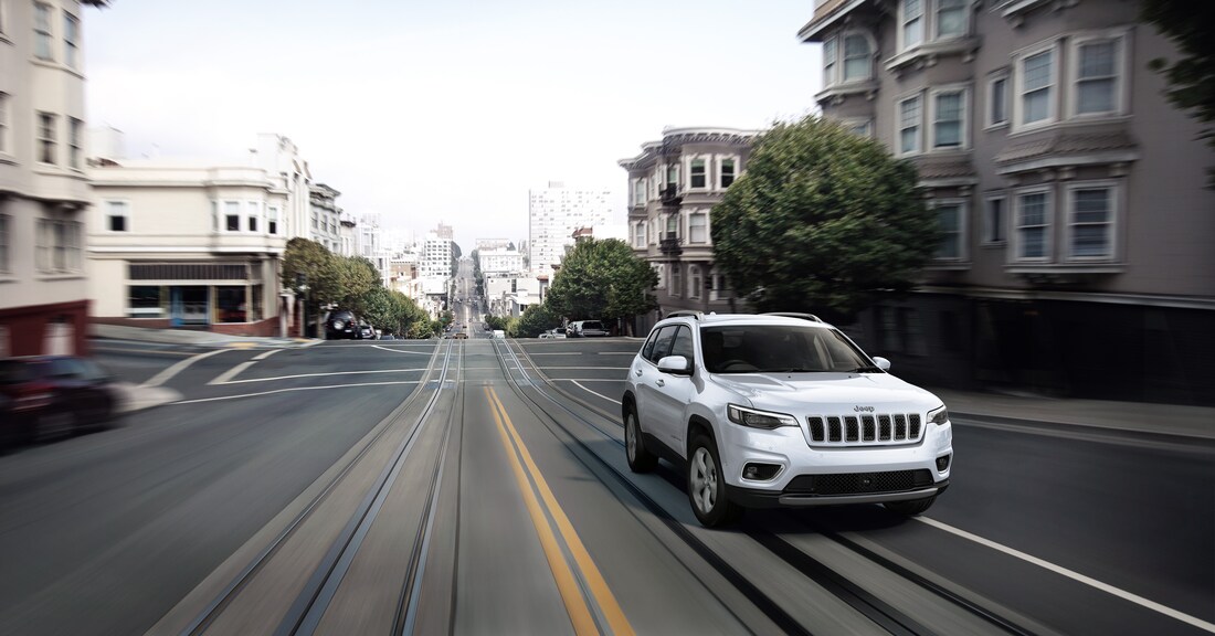 white Jeep Cherokee SUV driving fast down a city street