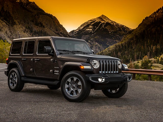 New Jeep Wrangler parked on a road surrounded by mountains with a sun set behind it.
