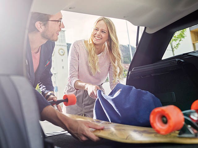 Two people are loading a vehicle with a skateboard and a bag.