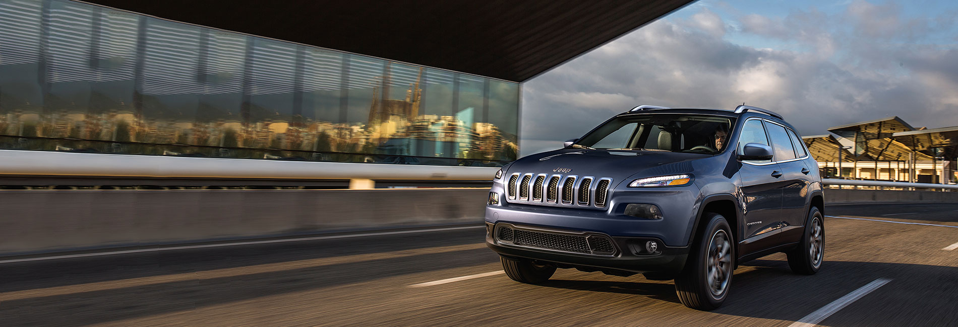 A new Jeep Cherokee driving on a bridge in a city.
