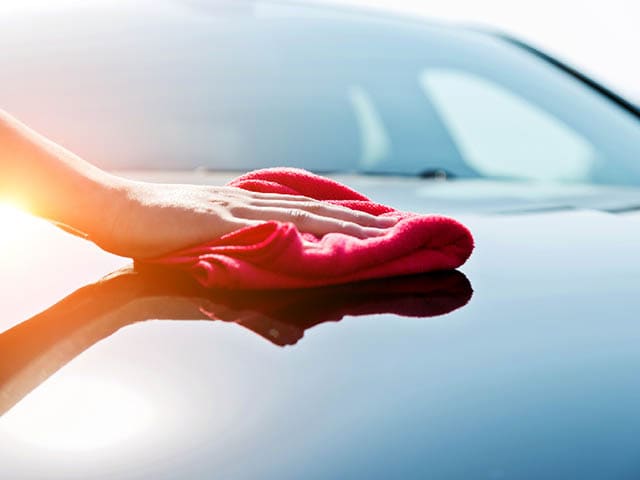 A hand holding a towel wiping down a vehicle.