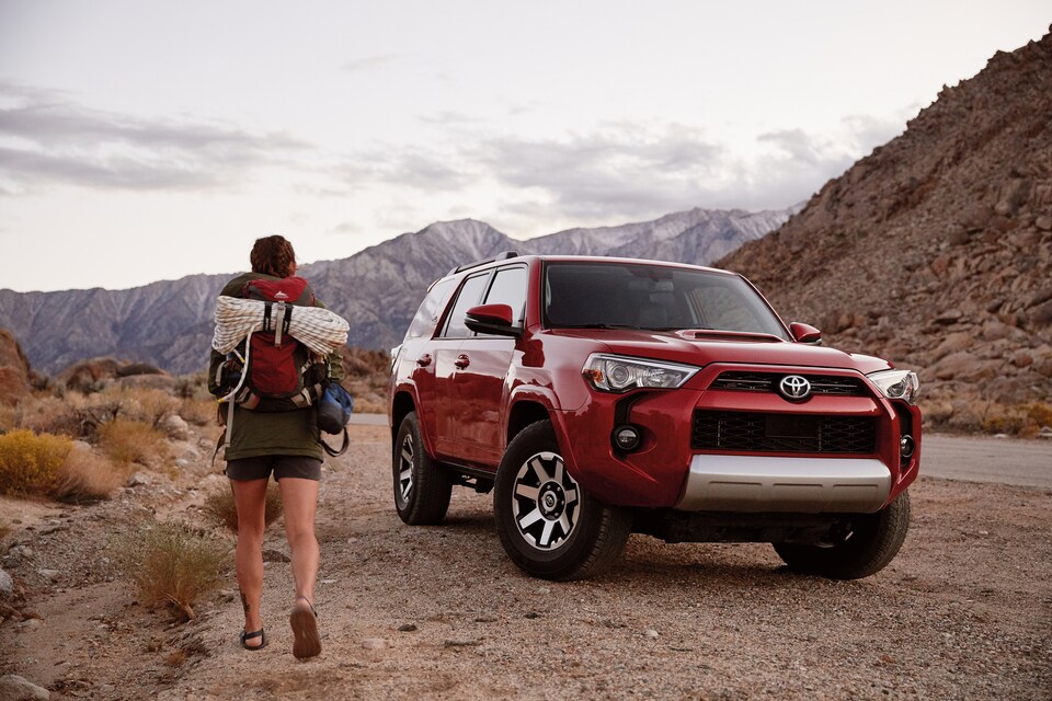 red Toyota 4Runner SUV parked in the desert with a backpacker walking by