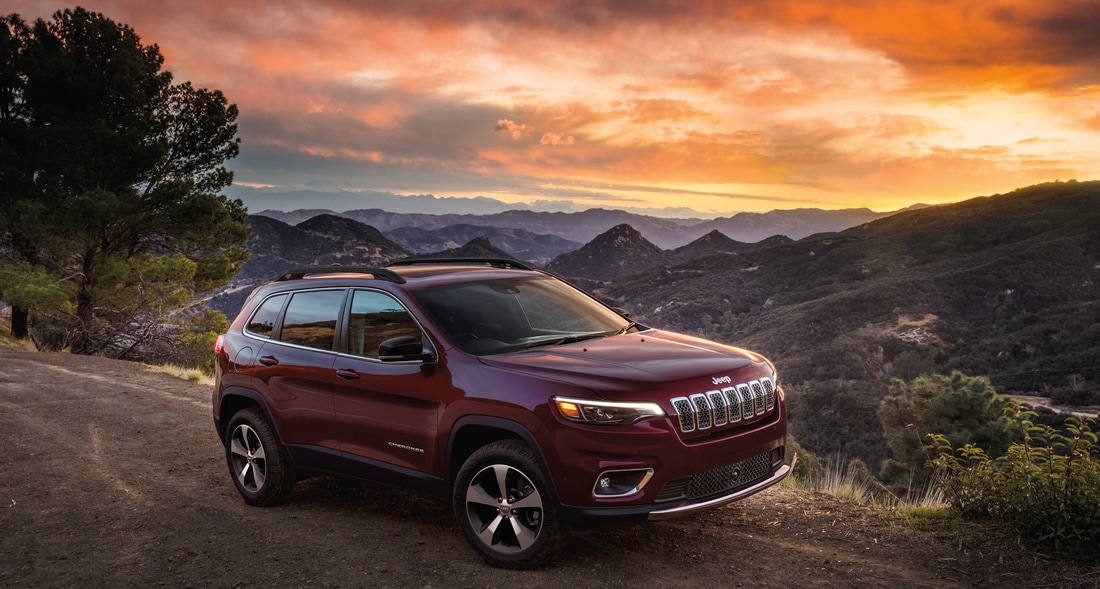 maroon Jeep Cherokee SUV parked on a dirt hill, overlooking a sunset