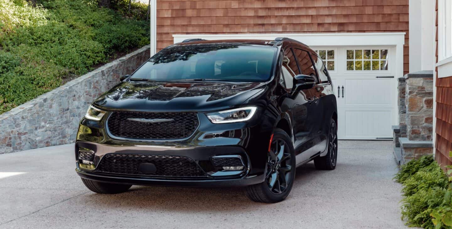 black Chrysler Pacifica hybrid minivan parked in front of a home