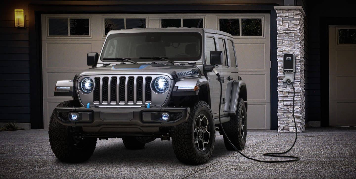 dark grey Jeep Wrangler 4xe hybrid SUV parked in front of a home, plugged into a charging station