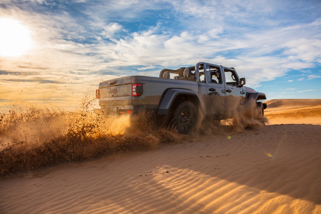 gray Jeep Gladiator truck kicking up sand, climbing up a hill