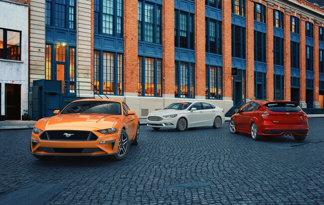 Ford vehicle lineup including an orange Ford Mustang, white Ford Fusion, and red Ford Edge