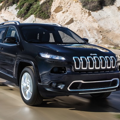 A new Jeep Cherokee driving on a road with a mountain behind it.