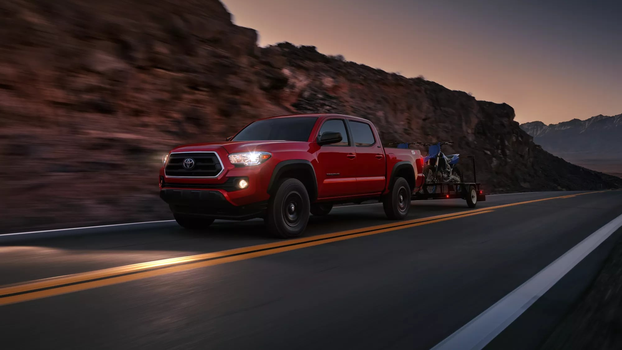 red Toyota truck driving near a rocky hill, towing ATVs