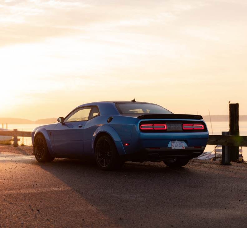 blue Dodge Challenger Hellcat coupe parked on a pier at sunset