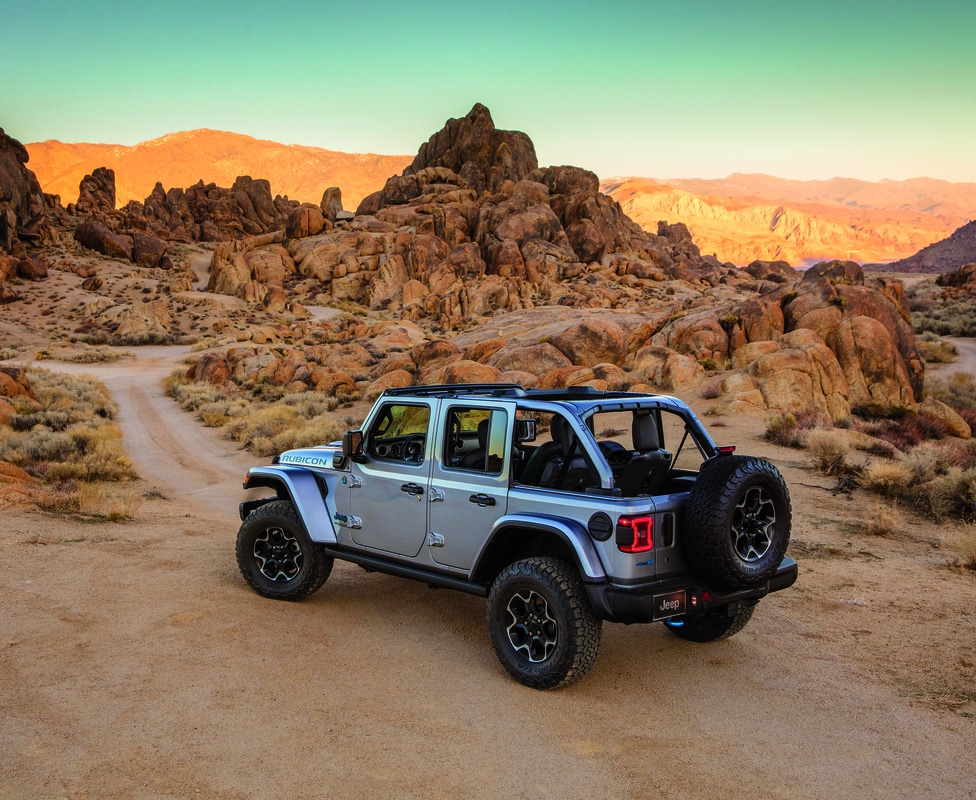 silver Jeep Wrangler 4xe hybrid SUV parked in a desert scene with the roof removed