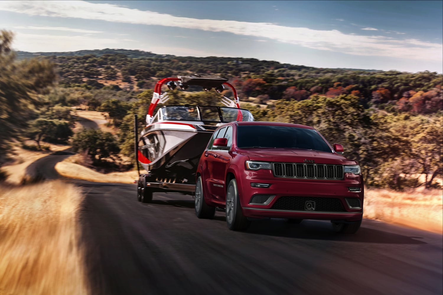 red Jeep Grand Cherokee SUV driving down a desert highway, towing a boat