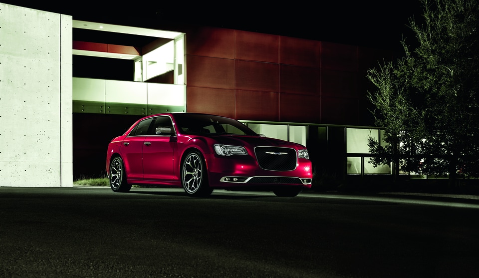 red Chrysler 300 sedan parked in front of a modern garage at night