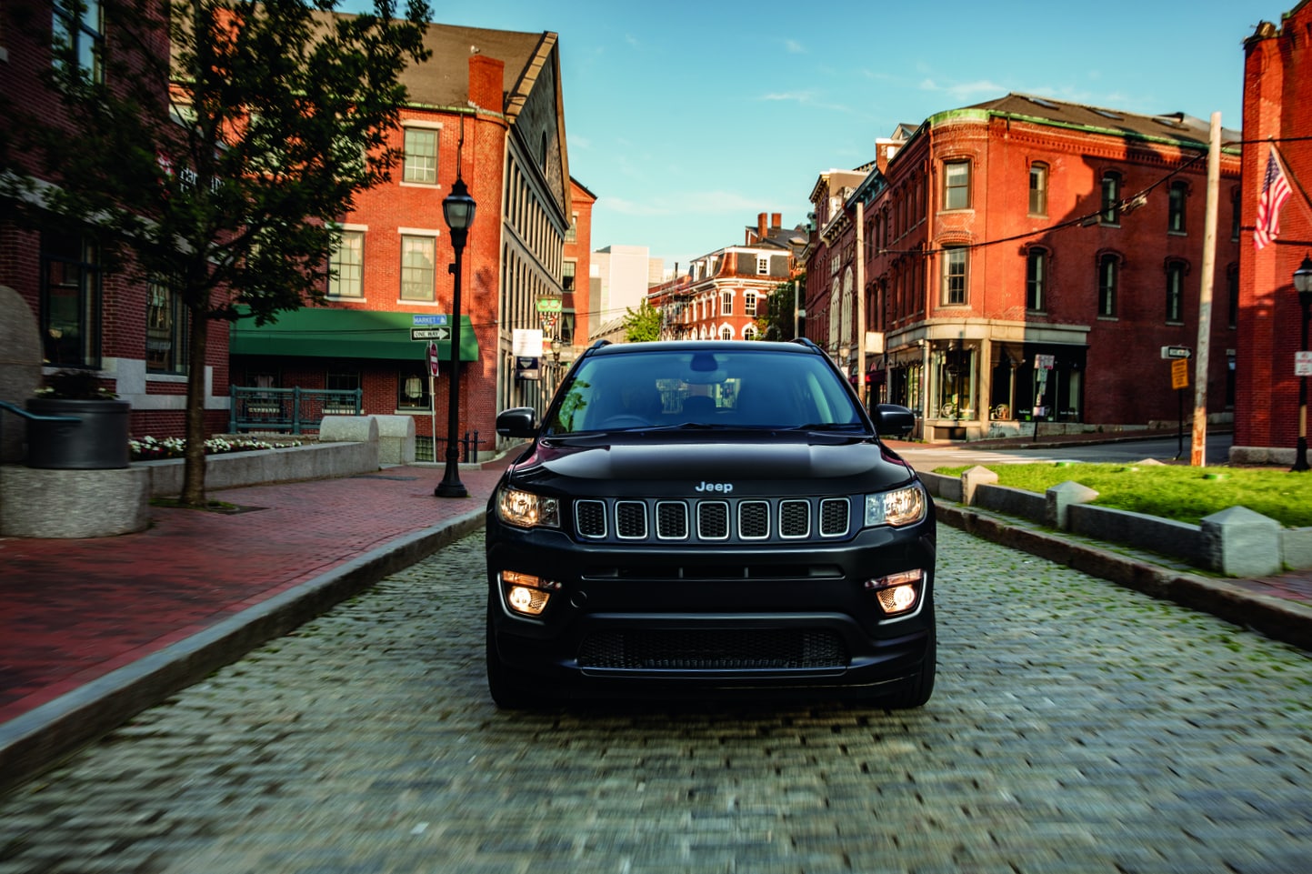 black Jeep Compass SUV parked, grill facing forward, parked on a cobblestone street