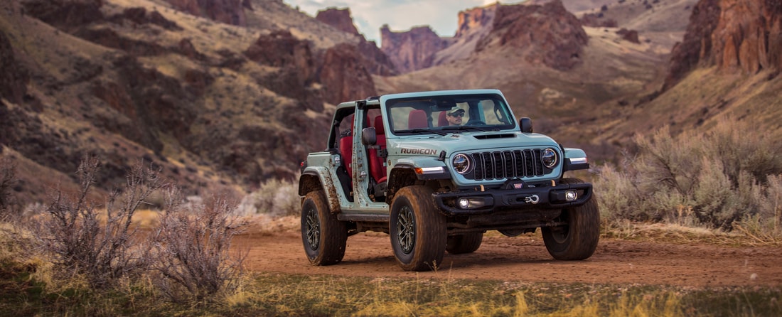 silver Jeep Wrangler Rubicon with no doors, driving through a red rock mountain area