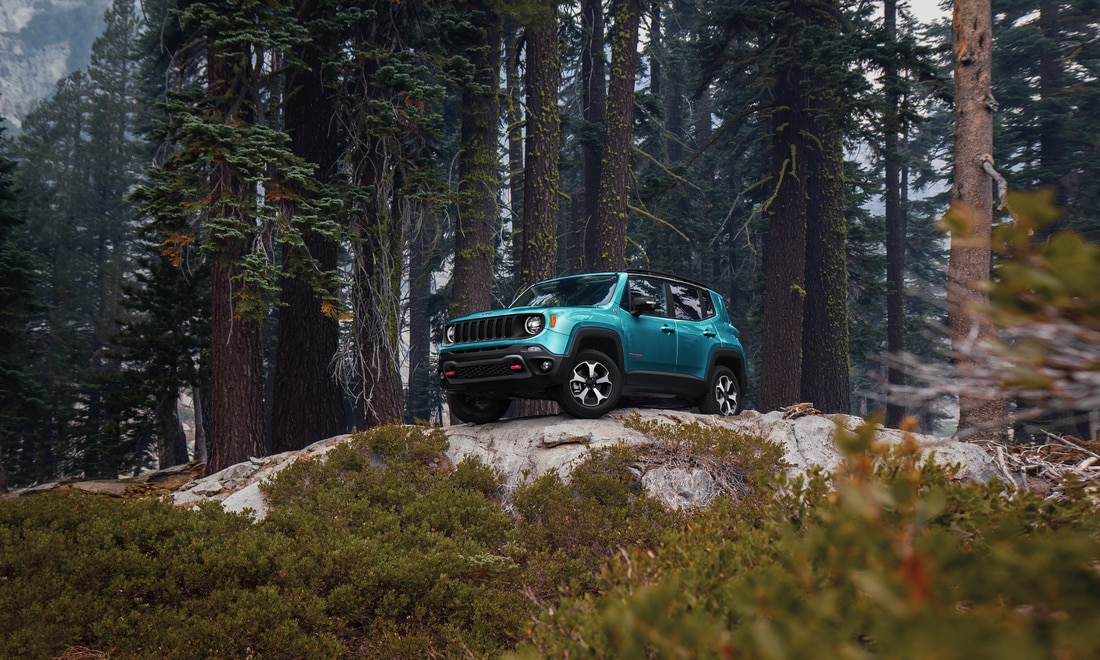 teal Jeep Renegade SUV parked on a rocky ridge in the forest