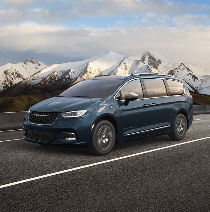 teal Chrysler Pacifica minivan driving down the highway with snowy mountains in the background