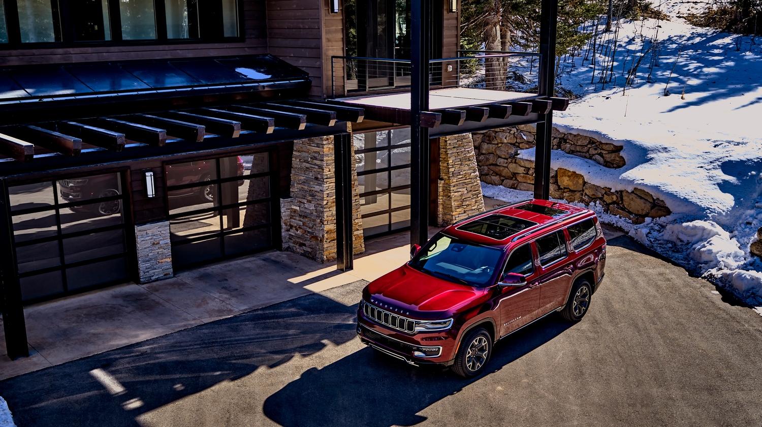 red Jeep Wagoneer SUV parked in front of a snowy lodge