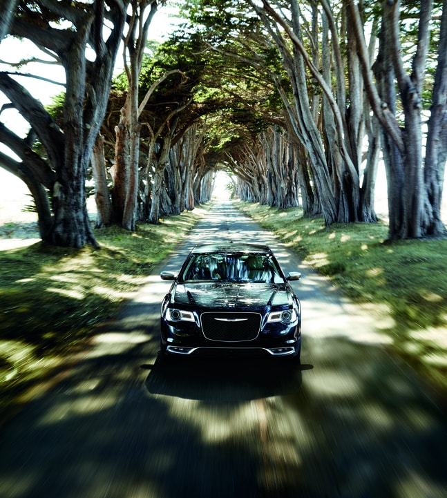black Chrysler 300 sedan driving down a tree-lined street