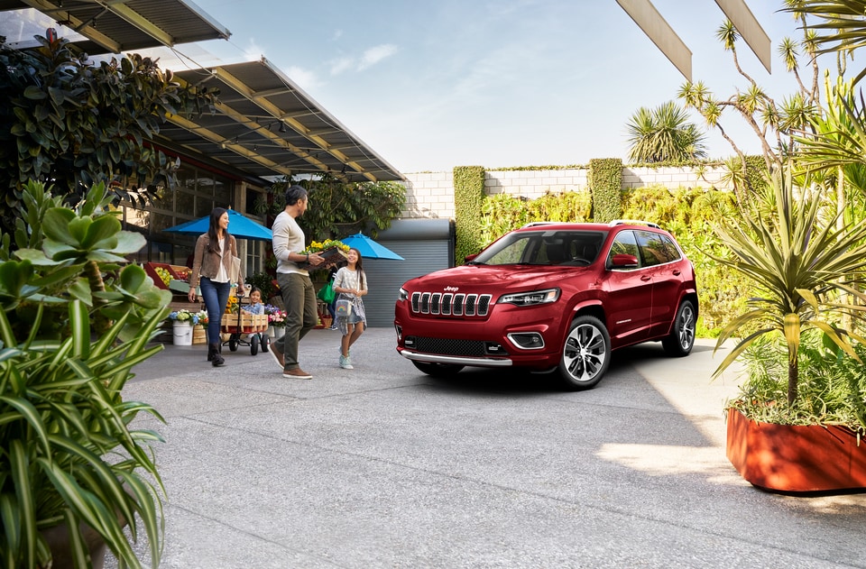red Jeep Cherokee SUV parked in front of a market with a family arriving