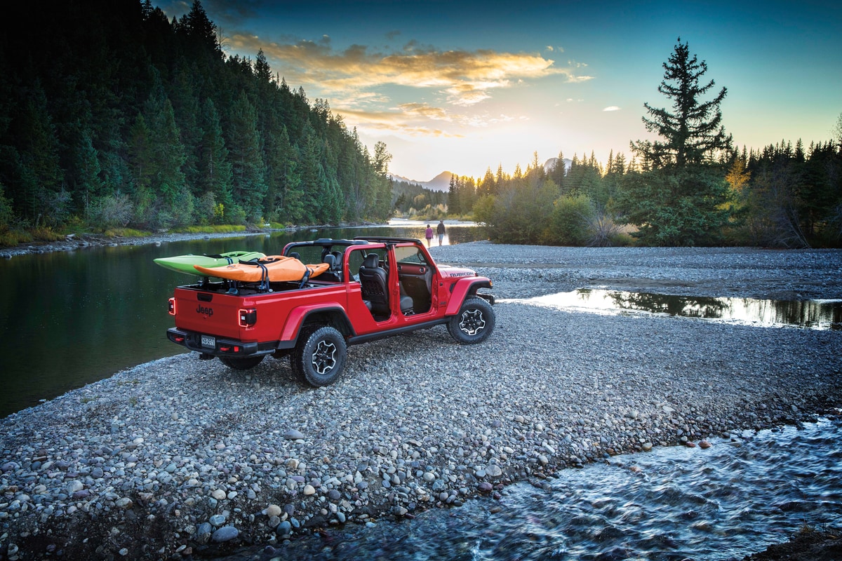 red Jeep Gladiator, loaded with kayaks, parked on a lakeside