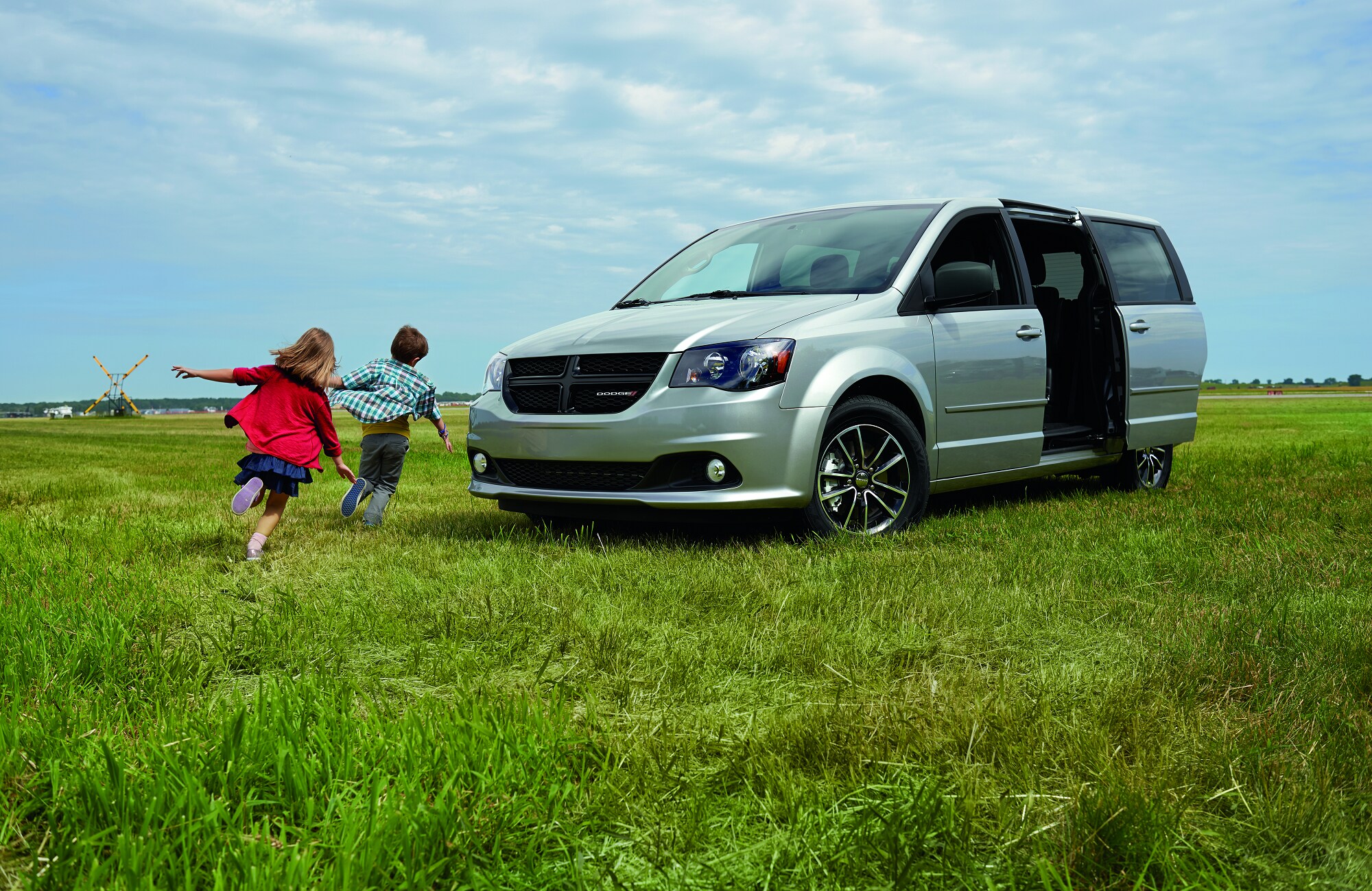 silver Dodge Grand Caravan Van parked on a grassy hill with kids playing nearby