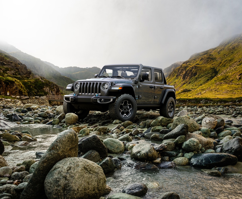 gray Jeep Wrangler bouldering over river rocks