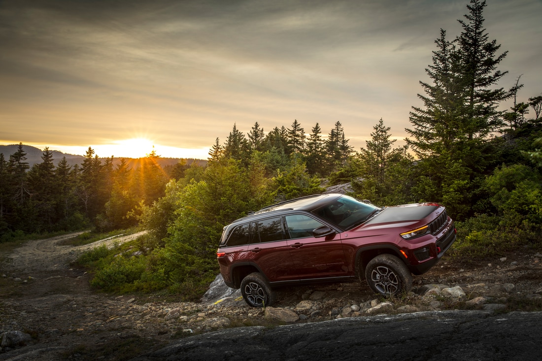 dark red Jeep Grand Cherokee SUV climbing up a steep hill with a stream