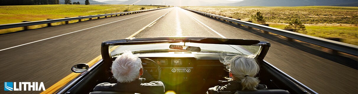 Senior couple driving convertible car at sunrise