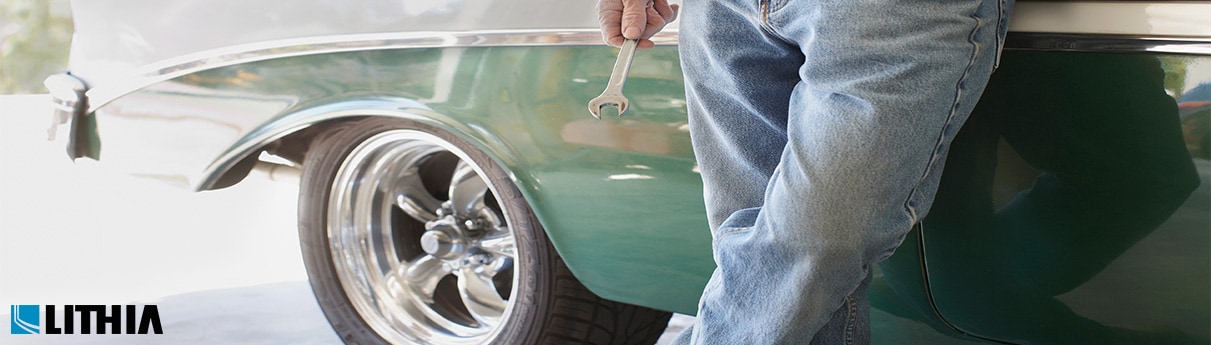 Man with wrench standing in front of older car