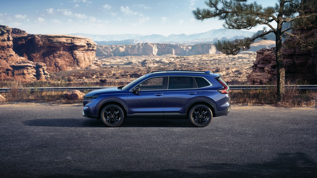 2025-Honda-CRVHybrid-SportTouring-SUV-L03.png blue Honda CR-V SUV parked next to a desert ledge