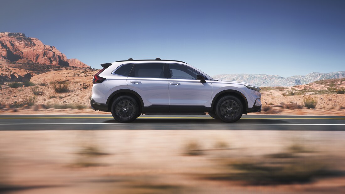 2025-Honda-CRVHybrid-SportTouring-SUV-L10.png white Honda CR-V Hybrid SUV driving on a desert road