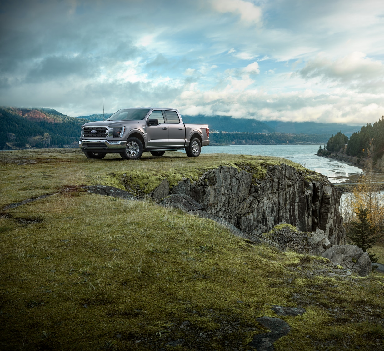 silver Ford F-150 truck parked on a rocky outcropping, overlooking a mountain river