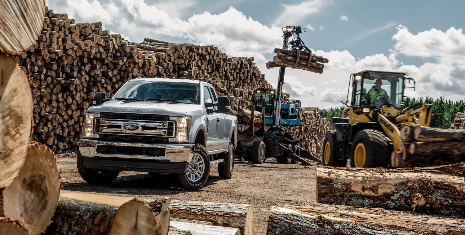 silver Ford F-350 truck receiving a load of logs from a small crane