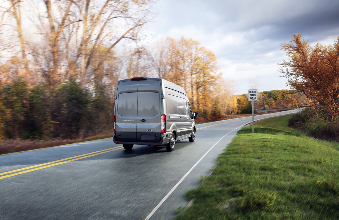 silver Ford Transit XL driving up a highway road