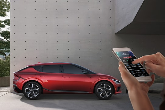 red Kia EV6 crossover SUV parked next to a cement wall with the driver starting it using an app