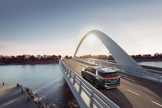 grey Kia Carnival driving over a stylized white bridge